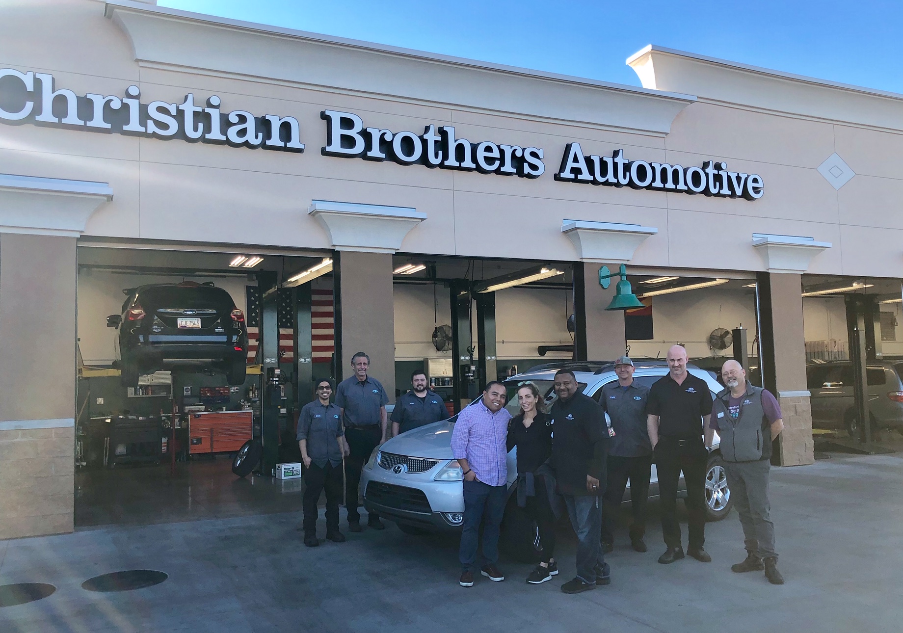 people in front of car in front of christian brothers automotive shop