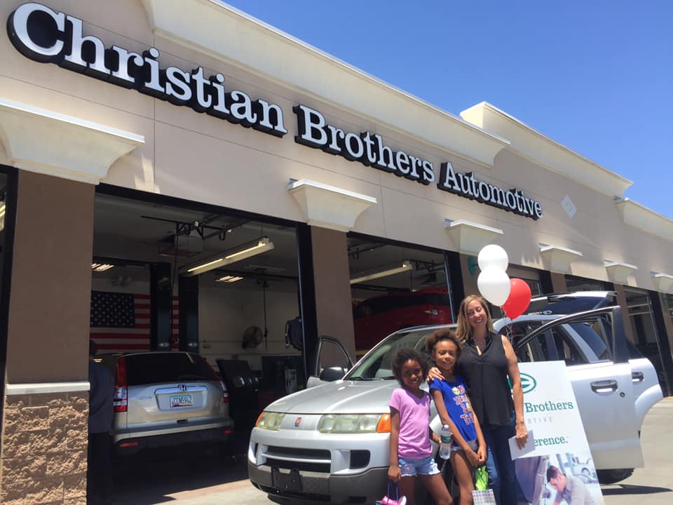 family in front of car in front of christian brothers automotive store